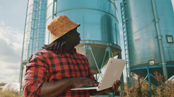 African Farmer Using Laptop in Front of the Silo Storage System