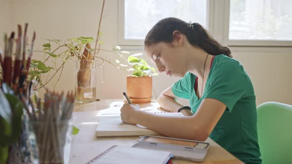 Teenage artist sitting drawing in a sketchbook in her room