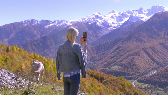 beautiful blonde takes photos or videos of a landscape in the autumn mountains.