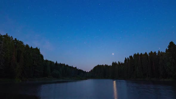 Night Sky with Clouds Illuminated By Stars Over a Mountain Lake and a Trees Silhouette