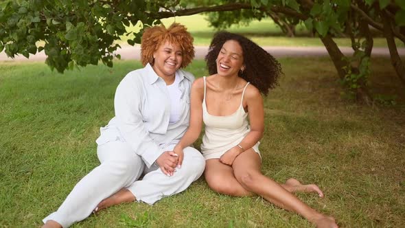 Lovely Beautiful Happy Lesbian African American Couple Sitting on Green Grass Hugging Outside at