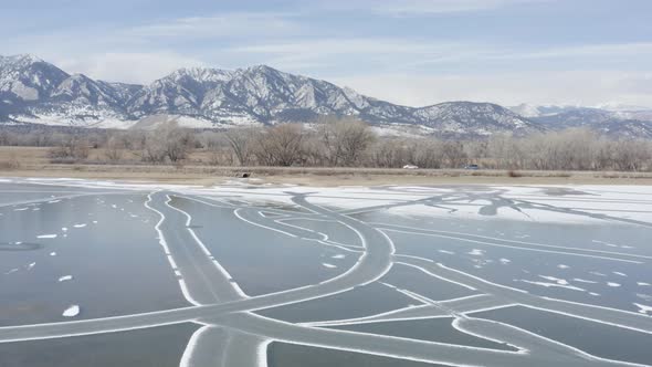 Cinematic Winter Aerial Flyover Ice Covered Frozen Lake Toward Rocky Mountain Road Boulder Colorado