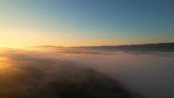 4K aerial view over mountain at sunrise in heavy fog. golden morning sunlight