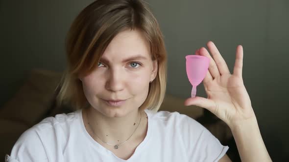 Young Woman is Showing Menstrual Cup and Laughing While Sitting at Home Room Iroi