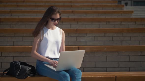 Smiling Woman Student Sitting on Bench Outdoors at the Street, Using Laptop Computer, Use Mobile