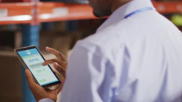 African american male worker with helmet using smartphone in warehouse