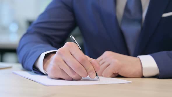 Close Up of Hands of Middle Aged Businessman Writing on Paper