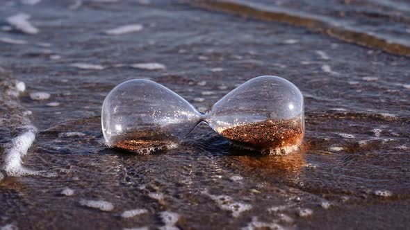 Waves Wash Sandglass Lying on Sand at Bright Summer Sunlight