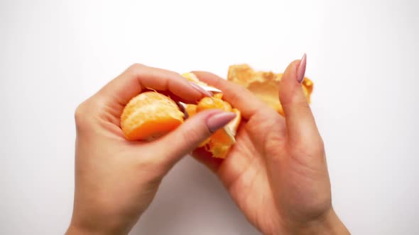 Hands clean tangerine with slices. Peeling process of mandarin on white background