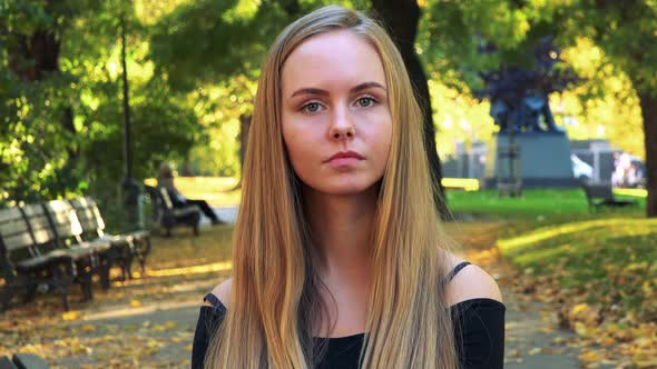 Young Beautiful Woman Looks To Camera with Serious Face in the Park