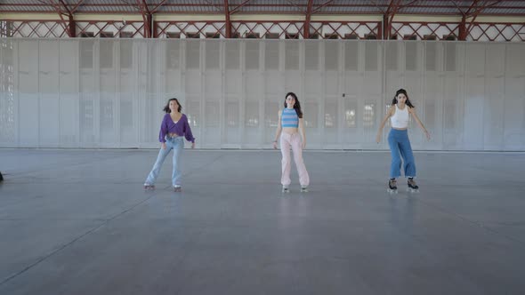 Three Young Women Roller Skate Toward Camera While Holding One Foot