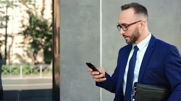 Trendy Businessman in Suit and Tie Use Smartphone Going Near Modern Building