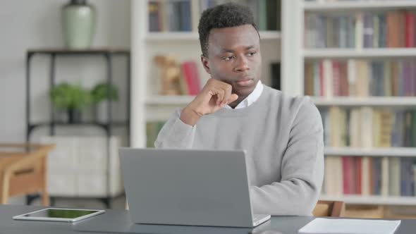 African Man Thinking While Working on Laptop in Library