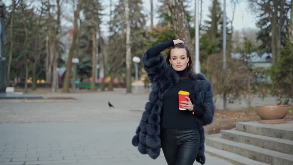 Beautiful young girl in luxury fur coat in the city park. 