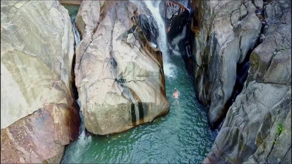 Aerial View Man Swims Across Blue Creek To Waterfall