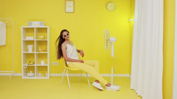 Young Woman Model Is Posing On Chair In Front of Electric Fan