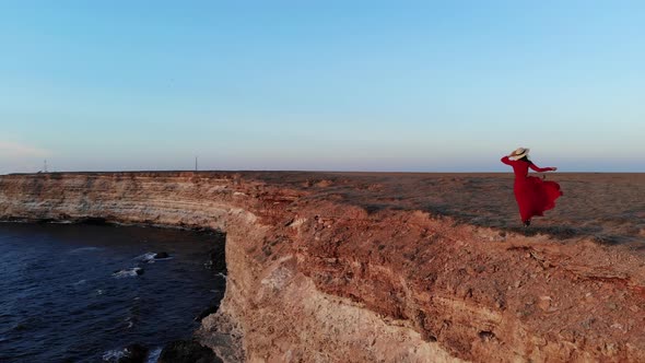 Aerial View of a Young Beautiful Woman in a Long Red Dress on a Mountain Rock Looking at the Sea a