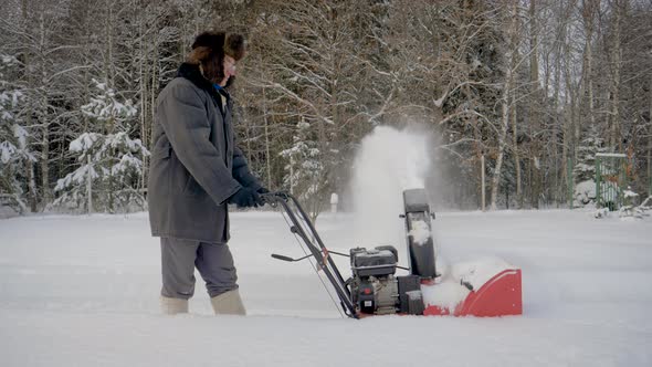 Man Cleans Road From Snow With Snow Plow On Background Of Forest In Winter