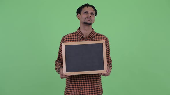 Happy Young Handsome African Man Thinking While Holding Blackboard