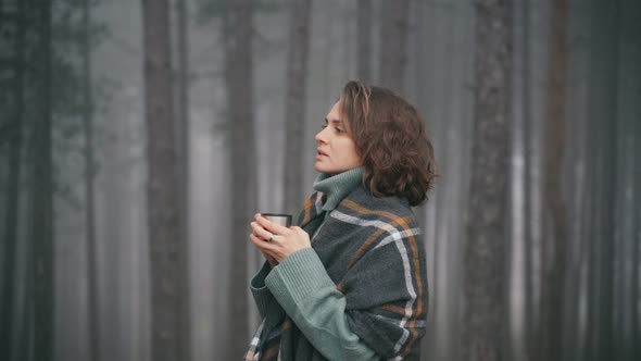 A Young Woman Wrapped in a Large Cozy Scarf Drinks Tea From a Thermos