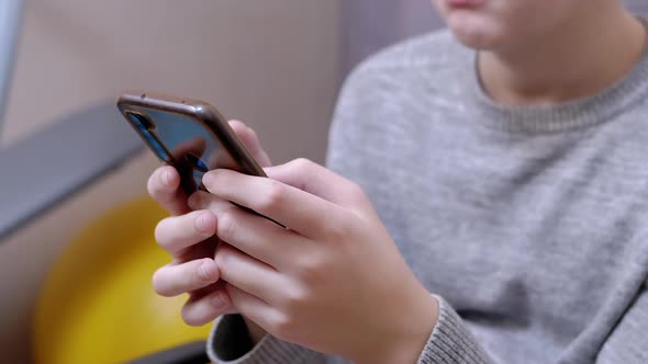 Child Sits in a Chair Holds a Smartphone in Hands Plays in Bedroom