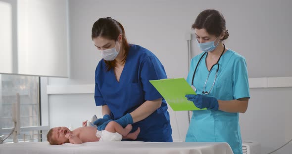 Doctor in Medical Mask and Gloves Making Ultrasound of Abdominal Cavity of Infant Baby
