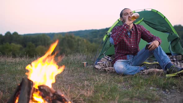 Man Traveling In Nature, Sitting Near Camp With Phone And Beer