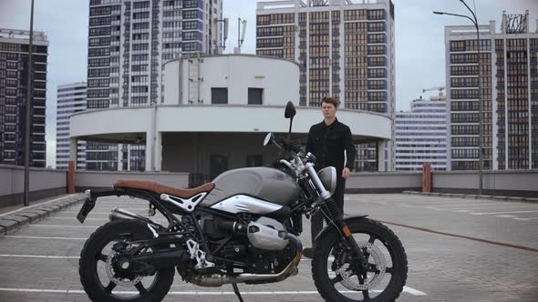 Man Comes to Scrambler Motorbike and Wears Helmet on Top of Multilevel Parking