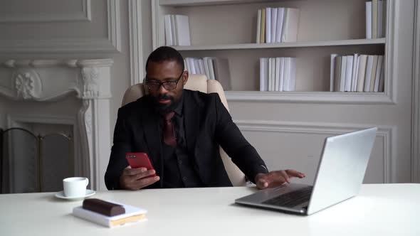 Busy Businessman Is Working in His Office, Black Man Is Sitting at Table with Laptop and Checking