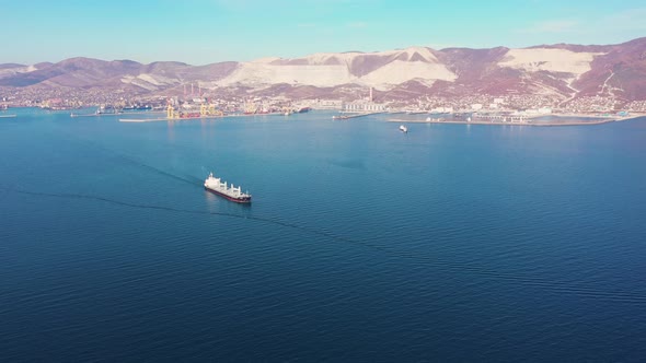 Aerial View Following the Ultra Large Cargo Ship at Sea Leaves Port at Sunset