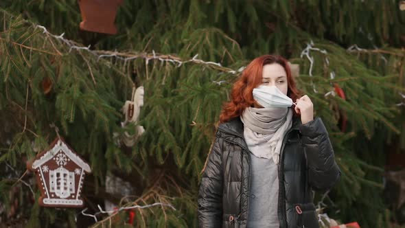 Tired Young Woman Takes Off Medical Mask Near Christmas Tree