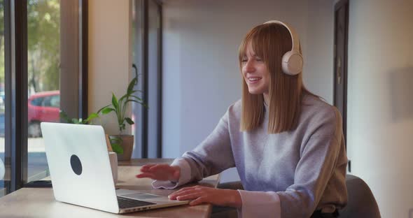 Young Blonde Woman Wint Headphone Using Computer During Conference Cal Sitting in Cafe