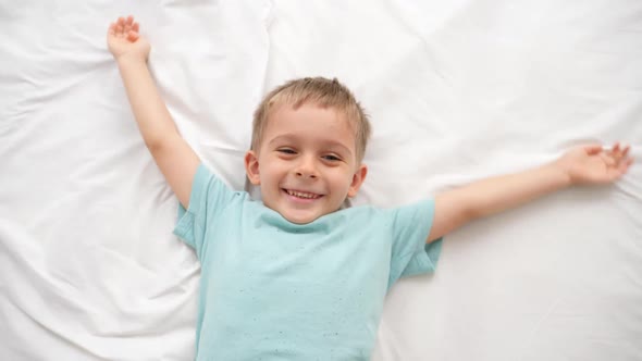 Top View of Happy Smiling Toddler Boy Lying on Bed and Waving with Hands Like Angel