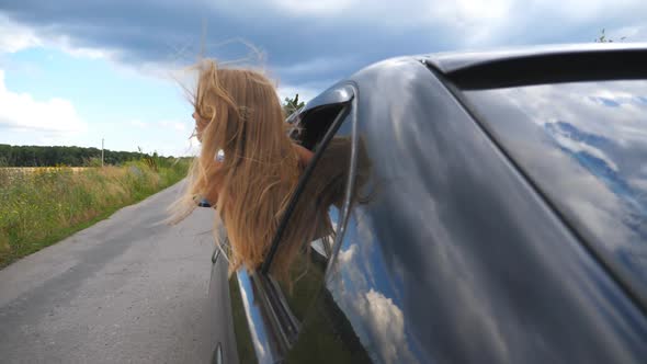 Beautiful Small Girl with Long Blonde Hair Leaning Out of Car Window While Riding Through Country