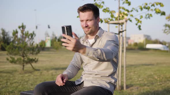 A Young Caucasian Man Talks on a Video Call on a Smartphone Waves His Hand and Smiles