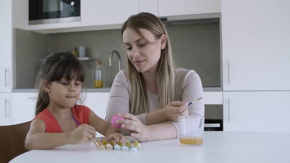 Mom Helping Little Girl To Paint Egg at Dining Table