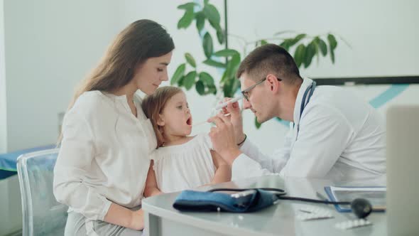 Male Doctor Pediatrician Examining an Ill Sad Kid at Medical Visit With Mother in the Hospital.