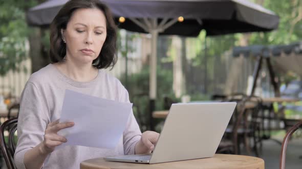 Paperwork By Old Woman Using Laptop in Outdoor Cafe