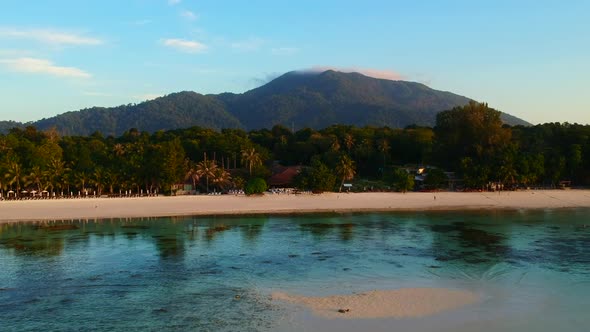 Distance and aerial footage of a white sand beach with green and mountain in the background