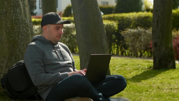 Young Man is Sitting in a Park in a Tourist Place Working on a Laptop