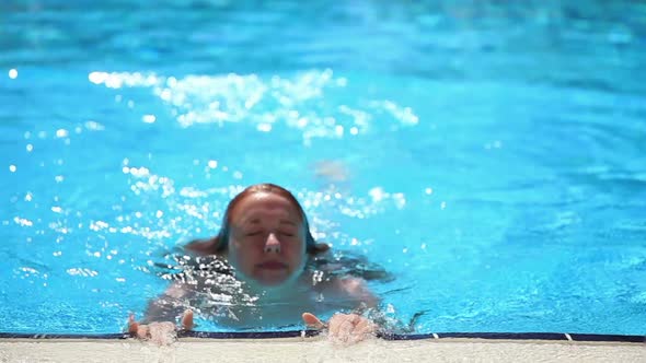 Beautiful Slim Girl with Red Hair Floats in the Pool and Smiles