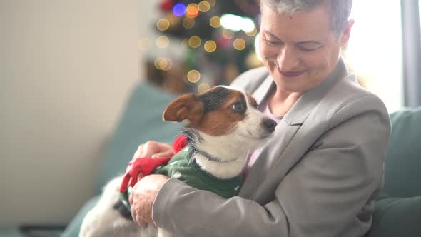 Beautiful Woman with a Short Haircut and Gray Hair Hugs Her Pet Puppy While Sitting on the Sofa