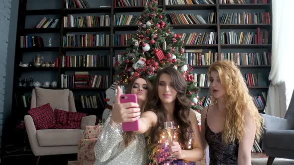 women in evening dres with glass of champagne take selfie near Christmas tree