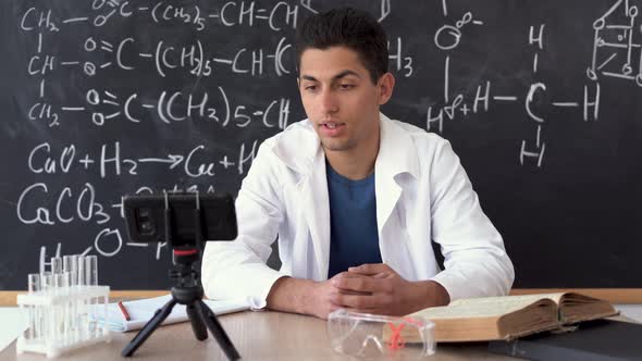 Young Modern Arab Chemistry Teacher in a White Coat During an Online Lesson Against a Blackboard