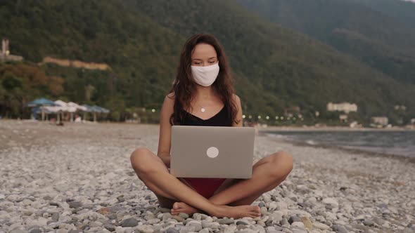 Young Business Woman in Bikini in Medical Mask Working on Laptop Alone By the Sea at the Beach