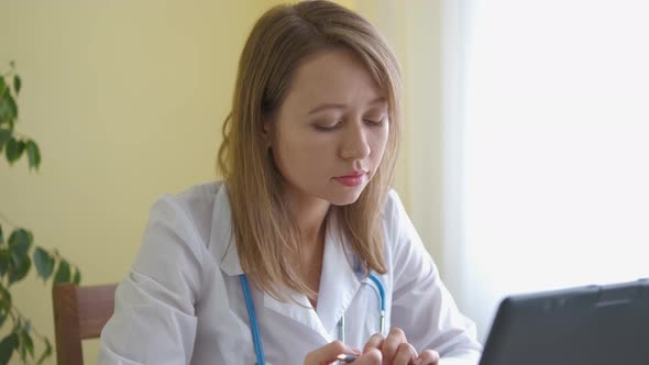 A nurse in a bathrobe and with a stethoscope works at a laptop