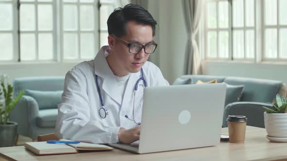 Asian Male Doctor Typing On Laptop Computer At Home Office