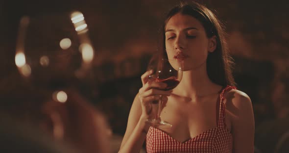 Young woman taking a sip from red wine and toasting with glasses