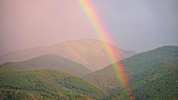 Beautiful rainbow forming from sun and rain storm on mountain hills. Time lapse.