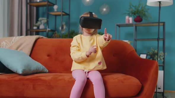 Toddler Girl Sitting on Home Sofa Using Virtual Reality Headset Helmet App to Play Simulation Game